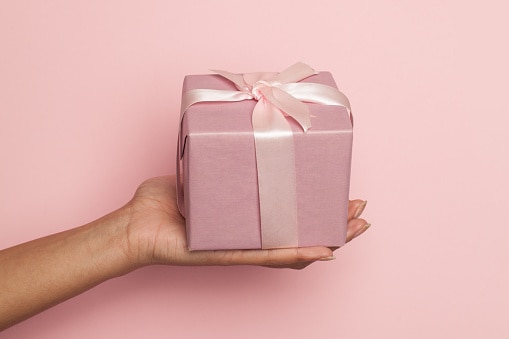 female hand holding gift with silky ribbon on pastel pink background